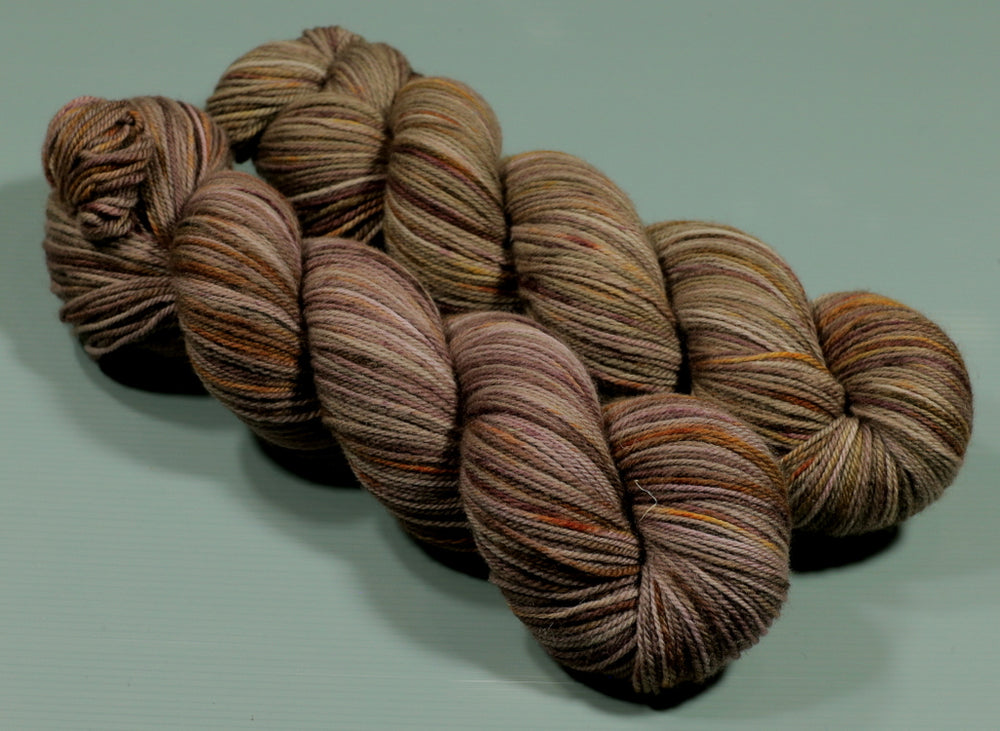 Two skeins fo autumn coloured yarn with beautiful highlights of gold an orange against a rich brown background